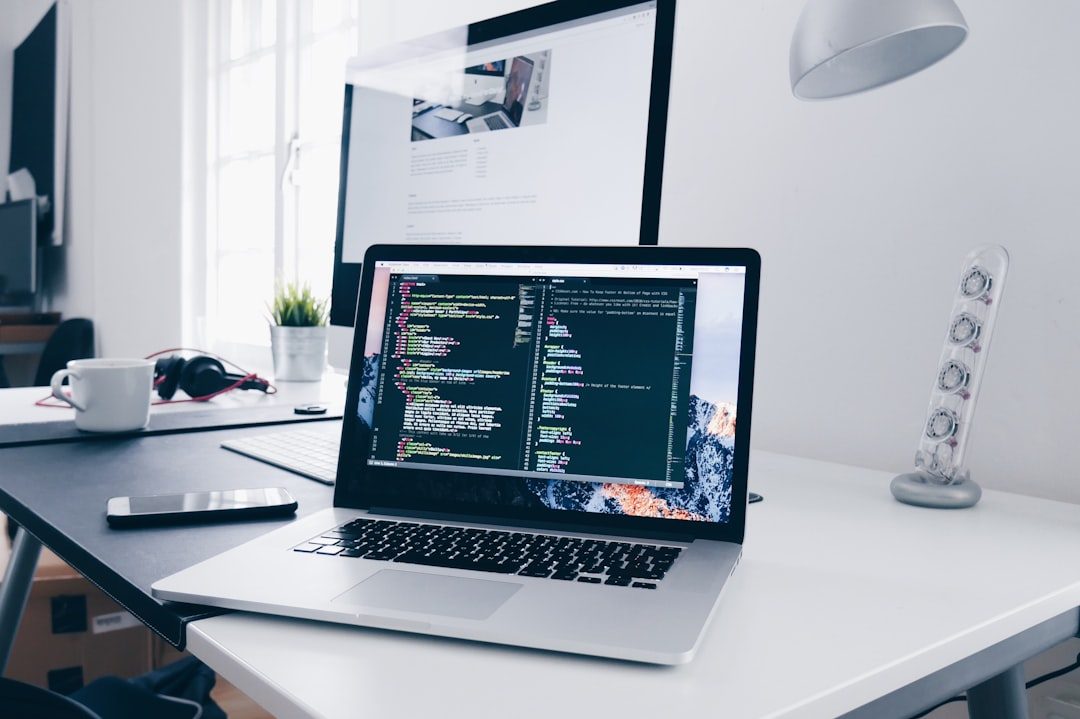 A MacBook with lines of code on its screen on a busy desk — aI-Native Applications Replace Bolt-On Features